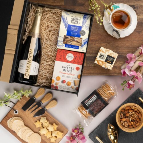 A symphony of colors and textures unfolds in this captivating flat-lay photograph, as an array of props encircle a gift hamper. The gift hamper holds an enchanting array of carefully selected surprises, each one contributing to a memorable and magical experience, filling the recipient's heart with wonder and creating a moment of pure enchantment. This gift hamper contains: Biscuits; Crackers; Sparkling Wine; Chutney and Pastes