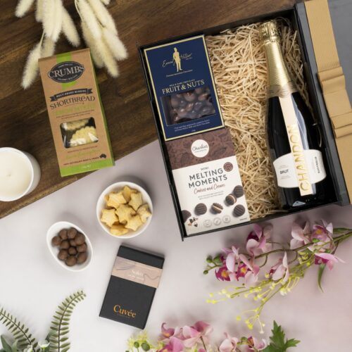 In this carefully composed flat-lay photograph, props of varying sizes and shapes are placed with precision, forming a beautiful frame for a gift hamper. Unbox the gift hamper to reveal a world of delightful items, each one chosen to create a memorable experience. This gift hamper contains: Biscuits; Chocolate; Sparkling Wine