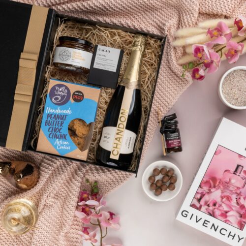 This stunning flat-lay composition showcases a symphony of props meticulously placed around a gift hamper. Explore the gift hamper and be amazed by the carefully curated assortment of delightful treats and luxurious treasures, offering a truly extraordinary experience. This gift hamper contains: Sparkling Wine; Chocolate; Biscuits; Jam