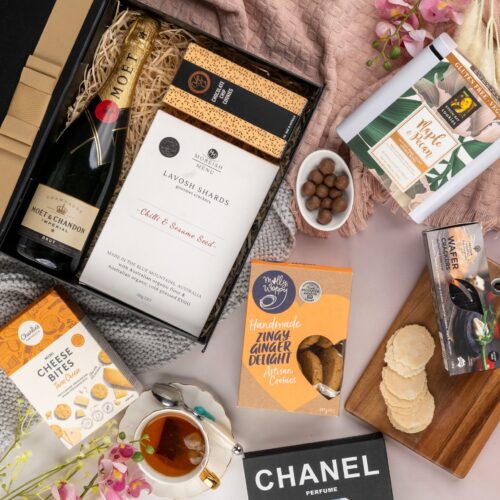 A harmonious blend of textures and colors characterizes this captivating flat-lay photograph, as props converge around a gift hamper. Open the gift hamper to uncover a meticulously chosen selection of items, each one contributing to a truly delightful experience, leaving the recipient in awe. This gift hamper contains: Crackers; Biscuits; Sparkling Wine