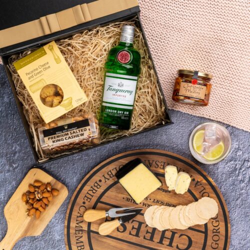 A feast for the eyes, this flat-lay photograph presents a carefully orchestrated tableau of props surrounding a gift hamper. The contents of the gift hamper promise a journey of indulgence and discovery, with each item carefully selected to bring joy and happiness, making every moment special. This gift hamper contains: Biscuits; Gin; Nuts; Antipasto