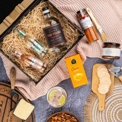 This striking flat-lay image features a curated selection of props that converge around a gift hamper, speaking of generosity and thoughtfulness. The contents of the gift hamper promise a journey of indulgence and discovery, with each item carefully selected to bring joy. This gift hamper contains: Jam; Tonic Water; Gin; Mustards and Dressings; Biscuits