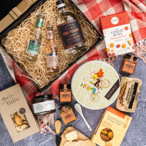A harmonious blend of textures and colors characterizes this captivating flat-lay photograph, as props converge around a gift hamper. Inside the gift hamper, you'll find a curated collection of wonderful items, each one chosen to bring joy and happiness. This gift hamper contains: Mustards and Dressings; Tonic Water; Nuts; Biscuits; Crackers; Gin; Jam