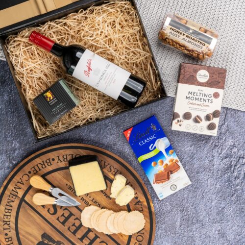 In this flat-lay photograph, a beautifully arranged assortment of props surrounds a gift hamper, creating an eye-catching composition. Inside the gift hamper, you'll find an exquisite selection of carefully chosen items, each one a delightful surprise. This gift hamper contains: Biscuits; Chocolate; Red Wine; Nuts