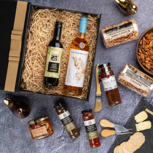 A symphony of colors and textures unfolds in this captivating flat-lay photograph, as an array of props encircle a gift hamper. Unveil the gift hamper to reveal a carefully selected assortment of delights, designed to captivate and impress. This gift hamper contains: Oil; Rose Wine; Mustards and Dressings; Nuts; Chutney and Pastes; Antipasto