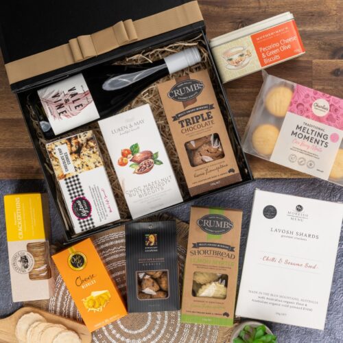 In this flat-lay photograph, a beautifully arranged assortment of props surrounds a gift hamper, creating an eye-catching composition. Unveil the gift hamper to reveal an assortment of carefully selected delights, guaranteed to impress. This gift hamper contains: Biscuits; Red Wine; Crackers