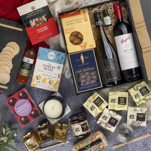 This visually arresting flat-lay image showcases a meticulously styled collection of props, expertly arranged around a gift hamper. The contents of the gift hamper promise a journey of indulgence and discovery, with each item carefully selected to bring joy and happiness, making every moment special and unforgettable, creating cherished memories to last a lifetime. This gift hamper contains: Jam; Honey; Chocolate; Red Wine; Biscuits; Candles; Chutney and Pastes; Crackers; Essential Oil; Nuts; White Wine; Diffuser