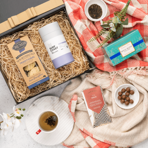 This meticulously styled flat-lay image showcases an array of props artfully positioned around a gift hamper, exuding a sense of excitement and intrigue. The contents of the gift hamper promise a journey of indulgence and discovery, with each item carefully selected to bring joy and happiness, making every moment special and unforgettable. This gift hamper contains: Biscuits; Tea (Black); Chocolate; Tea; Teaware