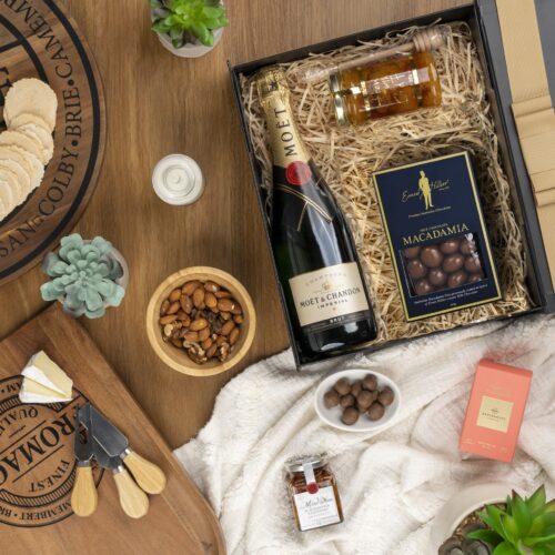 In this flat-lay photograph, a beautifully arranged assortment of props surrounds a gift hamper, creating an eye-catching composition. The contents of the gift hamper are a thoughtfully chosen selection of delightful treats and gourmet delicacies, a true gastronomic delight. This gift hamper contains: Honey; Sparkling Wine; Antipasto; Chocolate; Candles