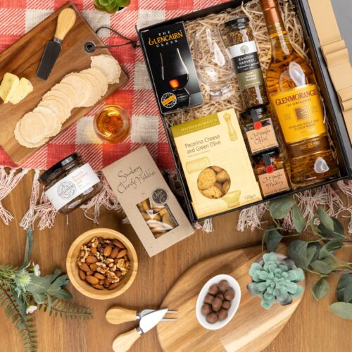 A carefully curated selection of props forms a picturesque frame around a gift hamper in this mesmerizing flat-lay photograph. Discover a captivating collection of items within the gift hamper, each one chosen with care and thoughtfulness. This gift hamper contains: Jam; Crackers; Mustards and Dressings; Antipasto; Whisky
