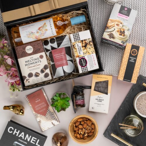 An artful arrangement of props weaves a story of anticipation and surprise in this captivating flat-lay photograph. Open the gift hamper to uncover a meticulously chosen selection of items, each one contributing to a truly delightful experience, leaving the recipient in awe and filled with gratitude, a gift that exceeds all expectations and touches the soul. This gift hamper contains: Rose Wine; Chocolate; Biscuits; Drinking Chocolate