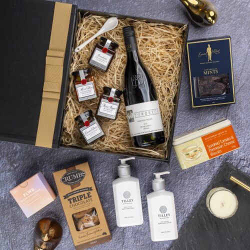 A meticulously arranged collage of props forms a picturesque backdrop for this flat-lay image, enhancing the allure of a gift hamper. Unbox the gift hamper to reveal a world of delightful items, each one thoughtfully selected to create a memorable occasion and leave a lasting impression, a true celebration of happiness. This gift hamper contains: Chocolate; Biscuits; Candles; Red Wine; Jam; Mustards and Dressings; Hand And Body Lotion