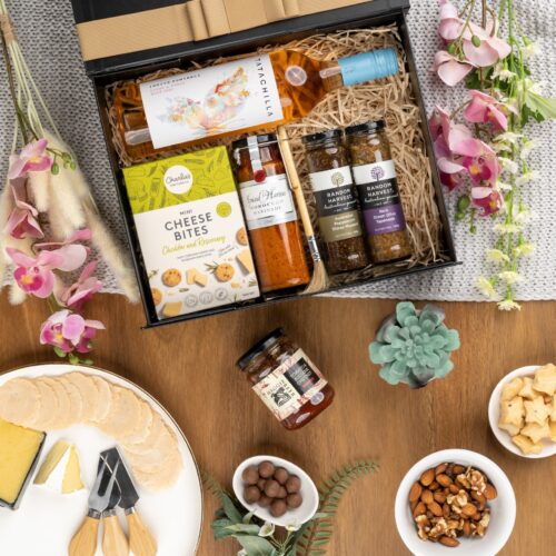 This stunning flat-lay composition showcases a symphony of props meticulously placed around a gift hamper. Unlock the gift hamper to reveal an array of delightful goodies waiting to be enjoyed. This gift hamper contains: Rose Wine; Mustards and Dressings; Biscuits; Chutney and Pastes