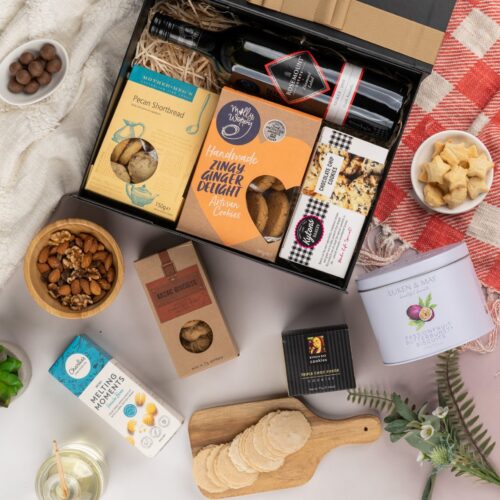 In this mesmerizing flat-lay composition, an assortment of carefully chosen props forms a visual tapestry around a gift hamper. Discover a captivating collection of items within the gift hamper, each one thoughtfully chosen to create a truly remarkable experience, taking the recipient on a journey of delight. This gift hamper contains: Biscuits; Red Wine