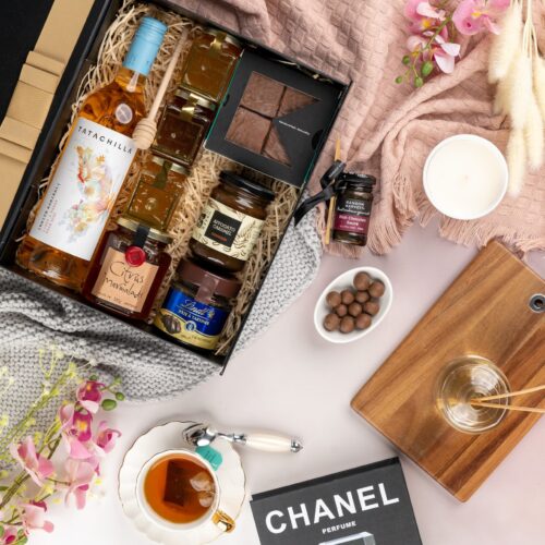 This captivating flat-lay composition entices the viewer with a carefully arranged assortment of props. Explore the gift hamper to find a delightful assortment of surprises, guaranteed to bring joy and excitement. This gift hamper contains: Chocolate; Rose Wine; Jam; Honey