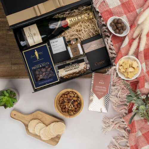 A visual symphony of colors unfolds in this mesmerizing flat-lay composition, as an assortment of props surrounds a gift hamper. Discover a carefully curated assortment of items nestled within the gift hamper, each one more delightful than the last. This gift hamper contains: Chocolate; Desert Sauce; Sparkling Wine
