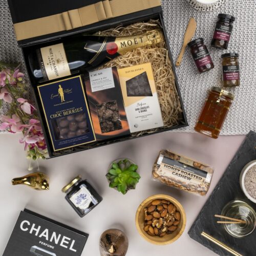 In this captivating flat-lay image, an array of carefully selected props encircles a gift hamper, creating a visual narrative. Explore the gift hamper and be amazed by the carefully selected assortment of delightful treats and treasures. This gift hamper contains: Chocolate; Sparkling Wine; Nuts; Honey; Desert Sauce; Jam