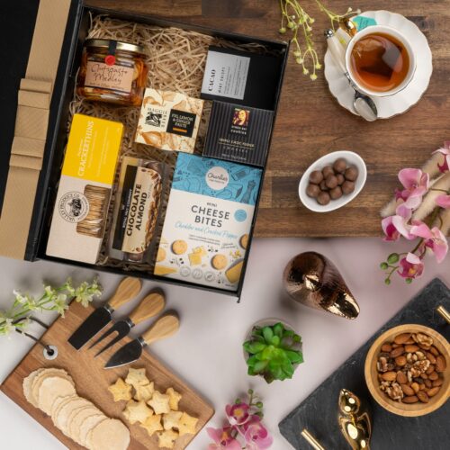 In this mesmerizing flat-lay composition, an assortment of carefully chosen props forms a visual tapestry around a gift hamper. The gift hamper is filled with an exciting variety of handpicked items, perfect for every occasion. This gift hamper contains: Biscuits; Crackers; Chutney and Pastes; Antipasto; Chocolate