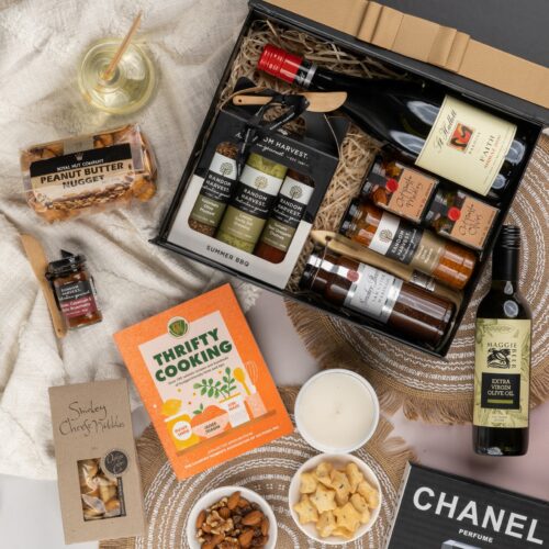 This captivating flat-lay composition entices the viewer with a carefully arranged assortment of props. Open the gift hamper to uncover a meticulously chosen selection of items, carefully arranged to bring delight. This gift hamper contains: Antipasto; Nuts; Cookbook; Mustards and Dressings; Chutney and Pastes; Red Wine; Oil