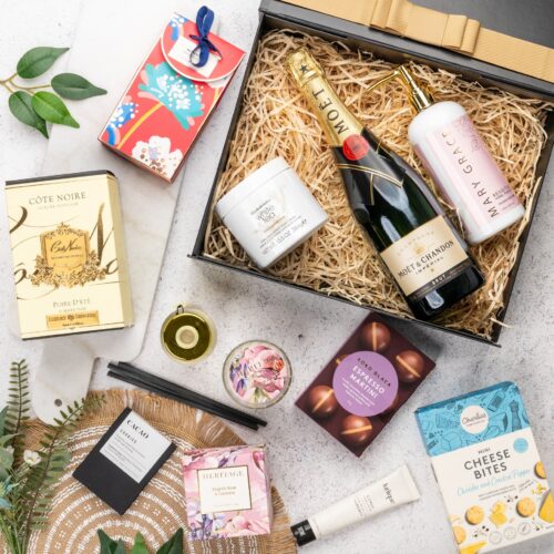 This captivating flat-lay image features a carefully curated collection of props arranged artfully around a gift hamper. Open the gift hamper to reveal a delightful surprise waiting to be savored, each item carefully selected to create a moment of pure bliss and bring a smile to the recipient's face, capturing their heart and filling their world with happiness, a gift that leaves an everlasting impression. This gift hamper contains: Sparkling Wine; Candles; Hand And Body Lotion; Body Cream; Hand Cream; Diffuser; Chocolate; Bath And Shower Gel; Biscuits