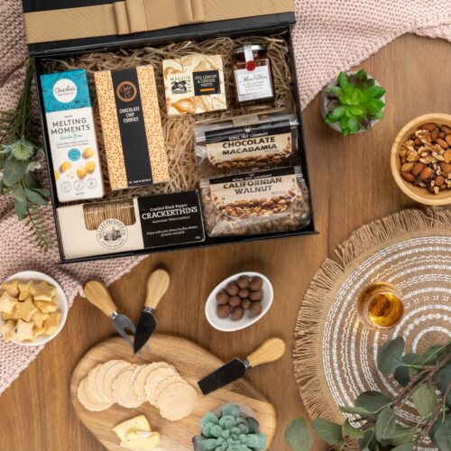An exquisite arrangement of props frames a gift hamper in this captivating flat-lay composition. The contents of the gift hamper are a collection of delightful treats and luxurious indulgences. This gift hamper contains: Antipasto; Biscuits; Nuts; Chocolate; Chutney and Pastes; Crackers