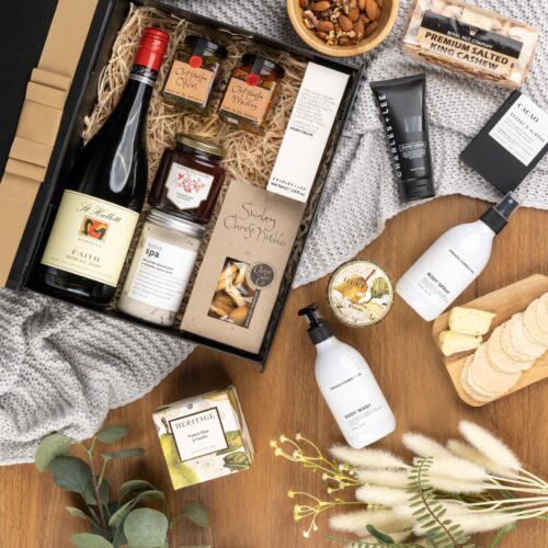 In this flat-lay photograph, a beautifully arranged assortment of props surrounds a gift hamper, creating an eye-catching composition. Explore the gift hamper and be amazed by the carefully curated assortment of delightful treats and luxurious treasures, offering a truly extraordinary experience. This gift hamper contains: Candles; Antipasto; Chocolate; Nuts; Jam; Skincare; Red Wine