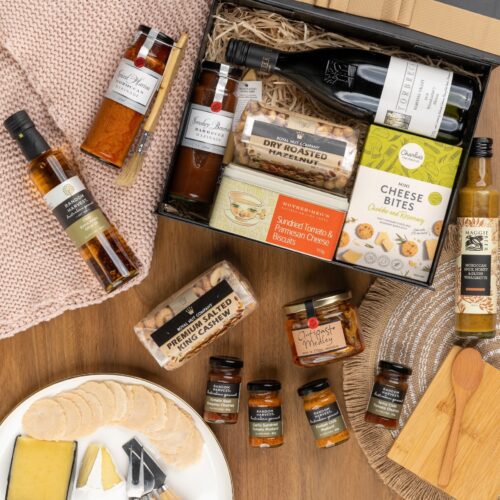 This striking flat-lay image features a curated selection of props that converge around a gift hamper, speaking of generosity and thoughtfulness. Explore the gift hamper and be amazed by the carefully curated assortment of delightful treats and luxurious treasures, offering a truly extraordinary experience that surpasses expectations, a gift that will be cherished forever. This gift hamper contains: Oil; Antipasto; Biscuits; Red Wine; Nuts; Vinegar; Chutney and Pastes; Mustards and Dressings